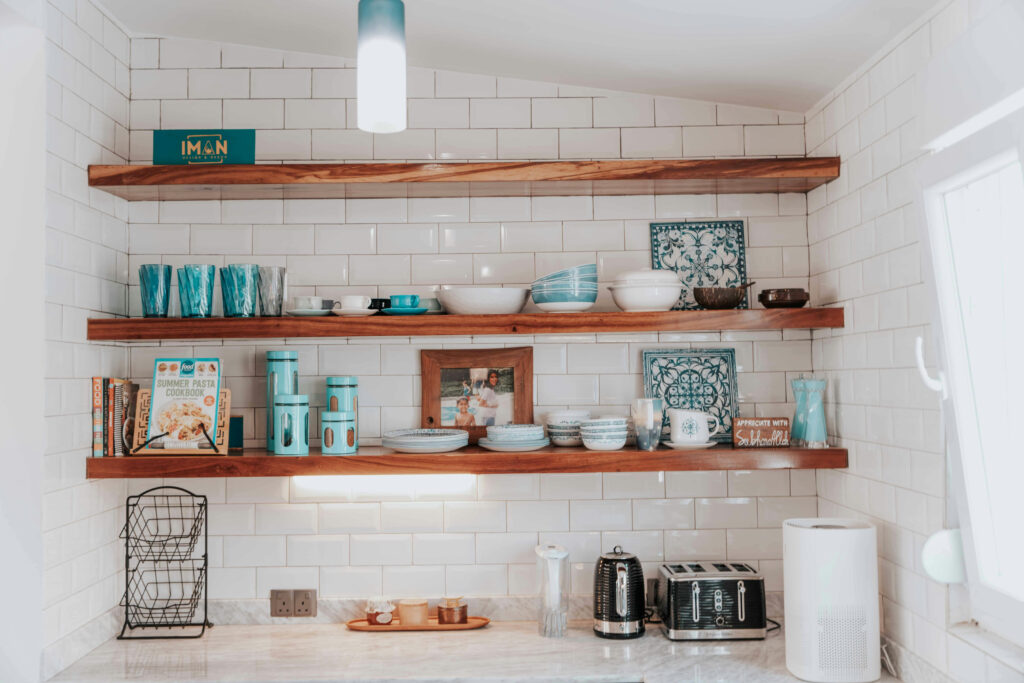 Stylish wood floating shelves organizing kitchen essentials and decor on a white tile wall