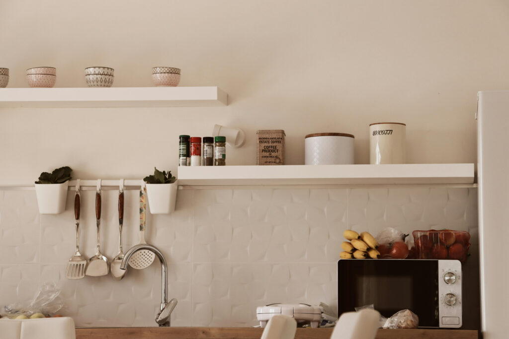 White floating shelves in a small kitchen with hanging utensils and spice jars