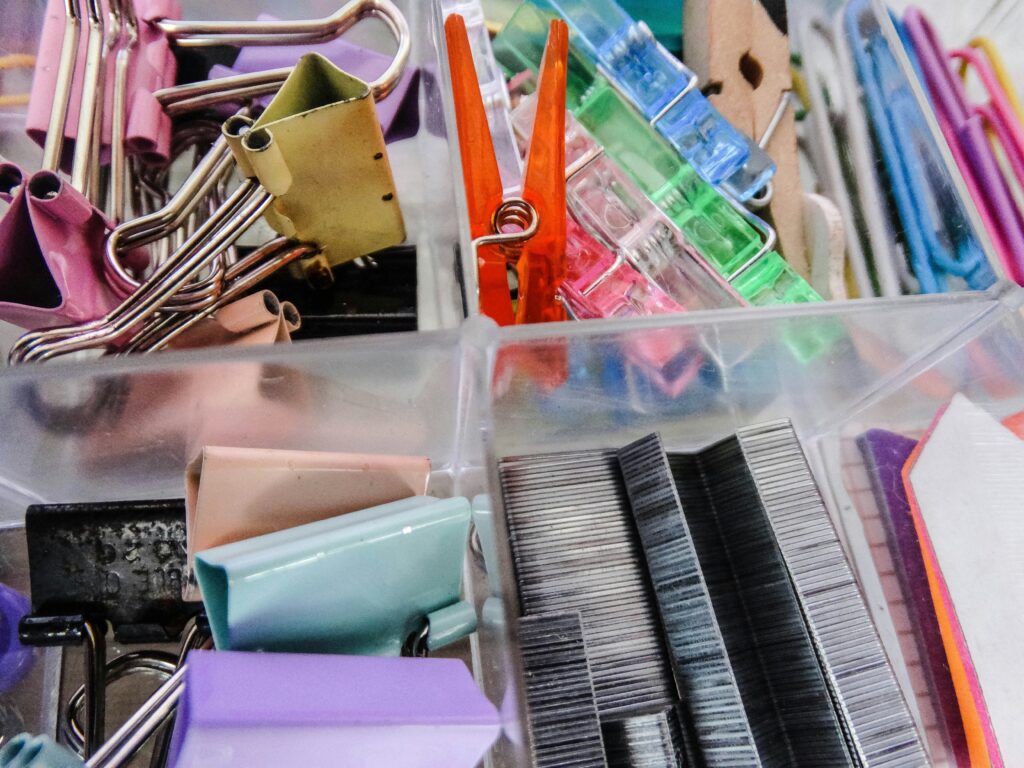Clear acrylic drawer organizer holding paperclips, staples, and binder clips.