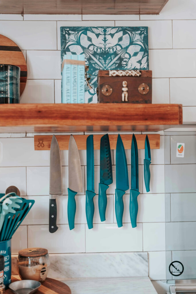 Wooden magnetic knife strip with teal knives on white tile wall