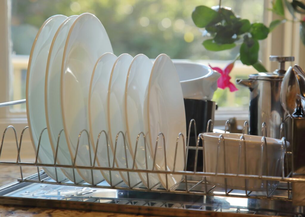 Stainless steel dish drying rack holding white plates on a sunny kitchen countertop