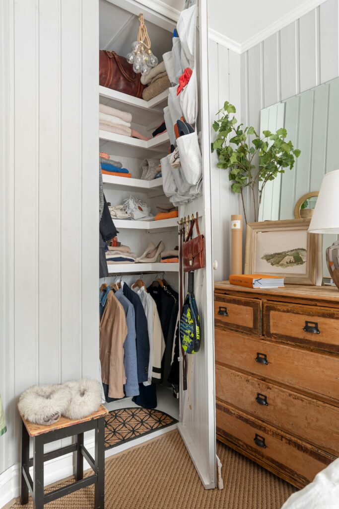 White closet with adjustable shelves and over-the-door hooks holding bags and accessories